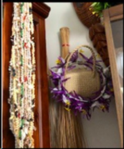 The picture displays a Cook Island 'ei katu (headpiece). It's mainly made of woven flax-like material, and has purple, yellow and white flowers or cloth around the brim