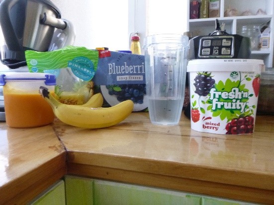 This is a picture of smoothie making ingredients on a bench top, including bananas, yoghurt and some blueberries